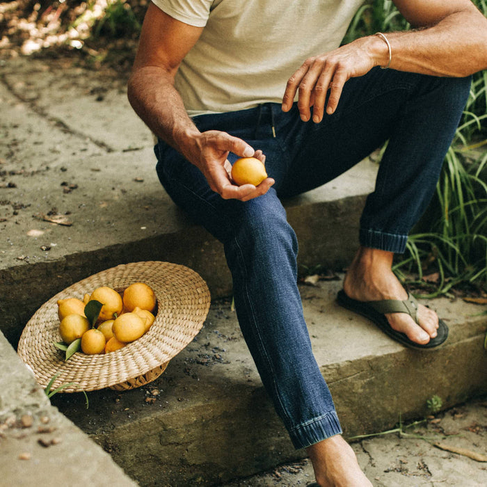 fit model wearing The Apres Pant in Indigo, sitting on steps holding lemon