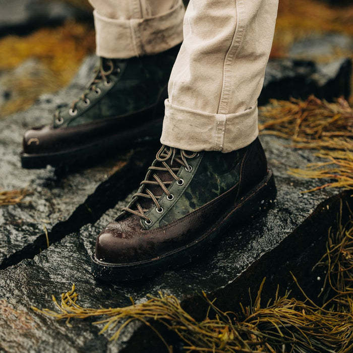 fit model standing on a rock wearing The Ridge Boot in Painted Camo
