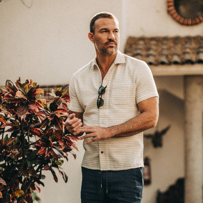 fit model wearingThe Short Sleeve Hawthorne in Natural Pickstitch Waffle, looking right, next to plant